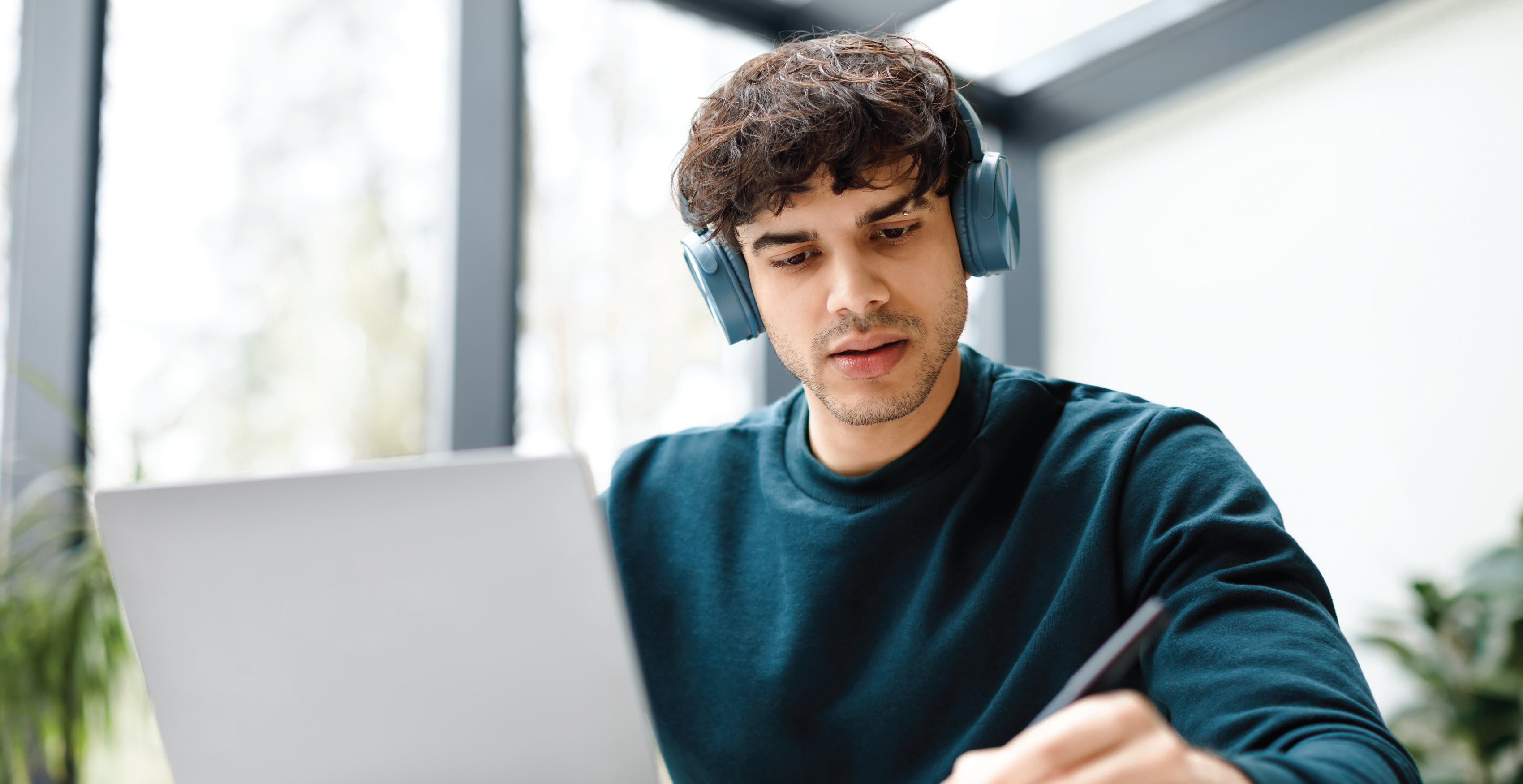 Student studying online with headphones while taking notes during a digital learning session.