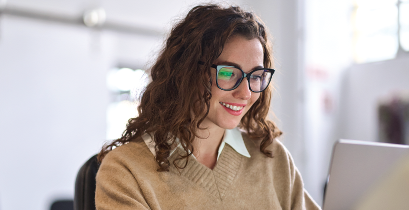 Student smiling while using a laptop for online learning in a bright study environment.