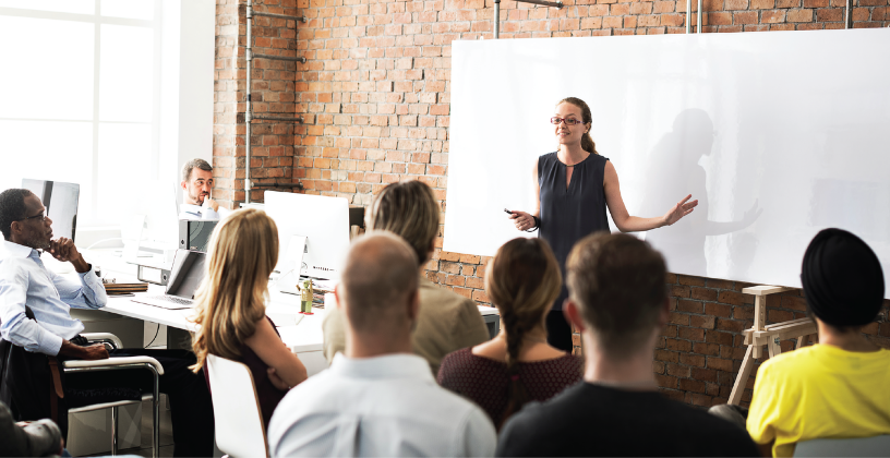 A woman presents to an audience, engaging them with her speech and visual aids in a conference setting.