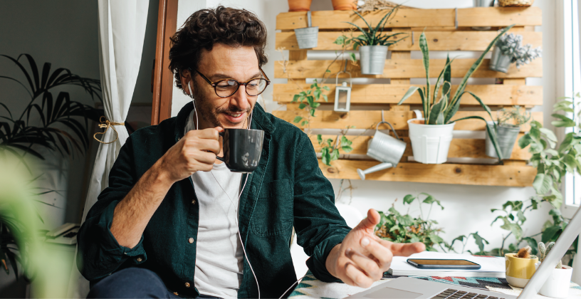 A man seated at a desk, working on a laptop with a cup of coffee beside him.