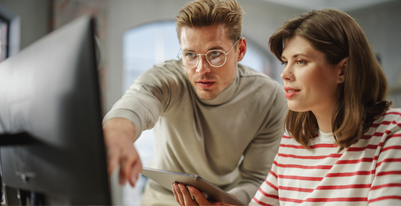 A man and woman collaborate while examining a computer screen together, discussing their work.