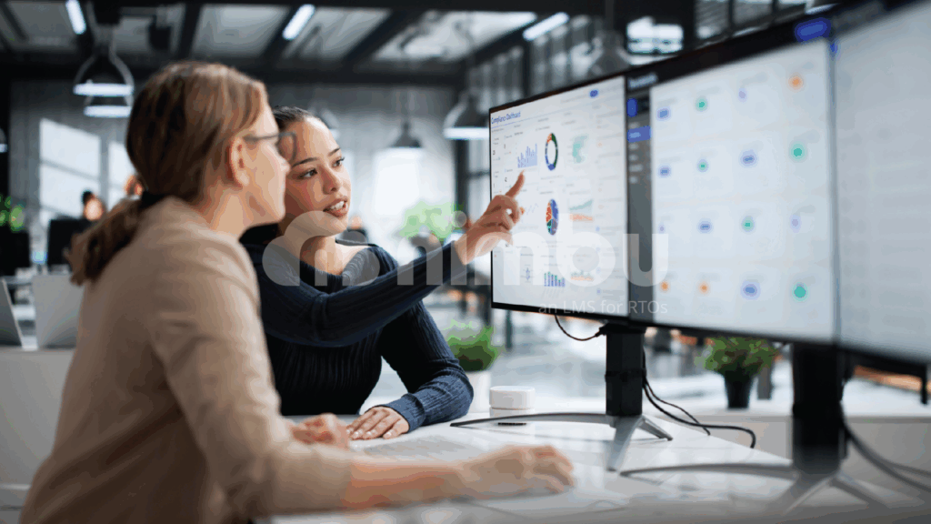 Two women collaborating at a computer in an office, focused on the screen and discussing their work.