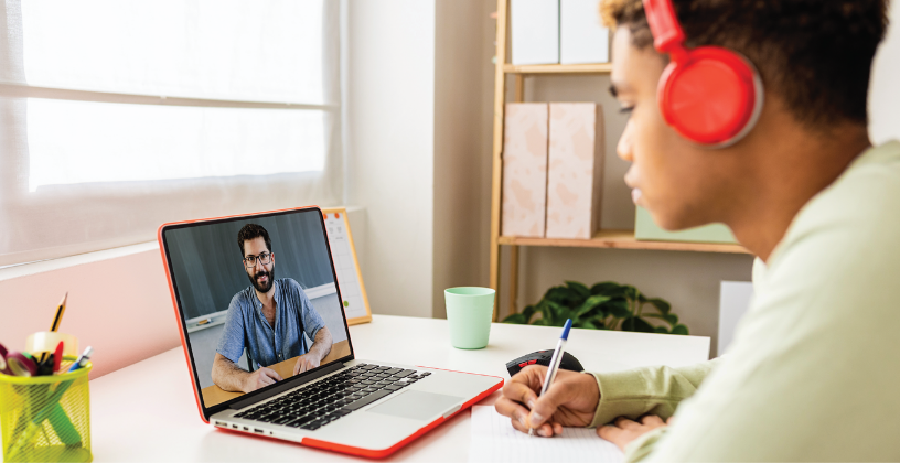 A man with headphones sits at a desk, focused on his laptop, engaged in work or a virtual meeting.